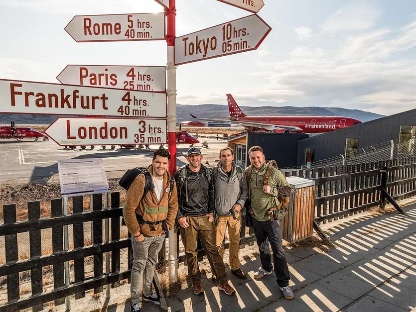 Renard, Nielsen, McKean and Meisel stand under a directional sign at the airport.