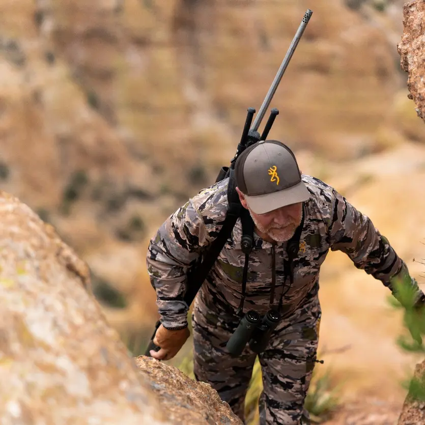 Whitetail deer hunter kneeling in field with X-Bolt rifle.