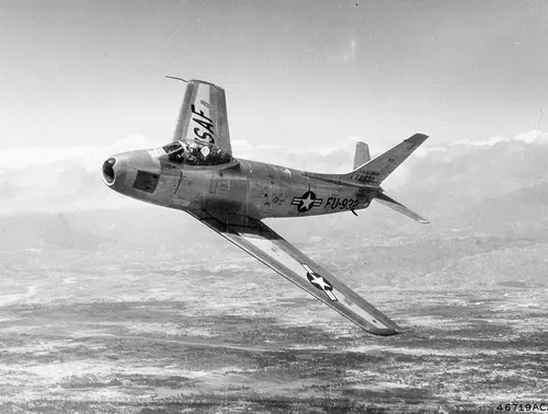 A USAF F86 Sabre banks to show three of its six Browning .50 caliber machine gun ports in the dark square on the side the fuselage, just forward of the cockpit. 